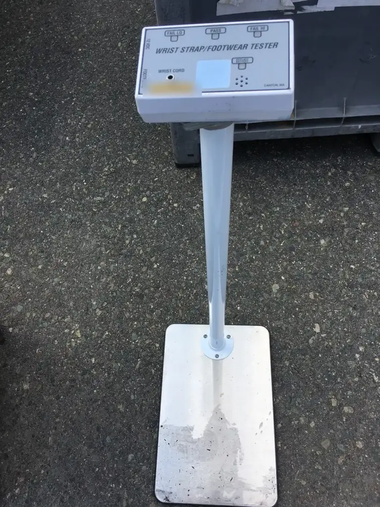 Comprobador de muñequeras y calzado antiestático, con una placa metálica en el suelo para subirse y un panel con luces de aprobado y fallo