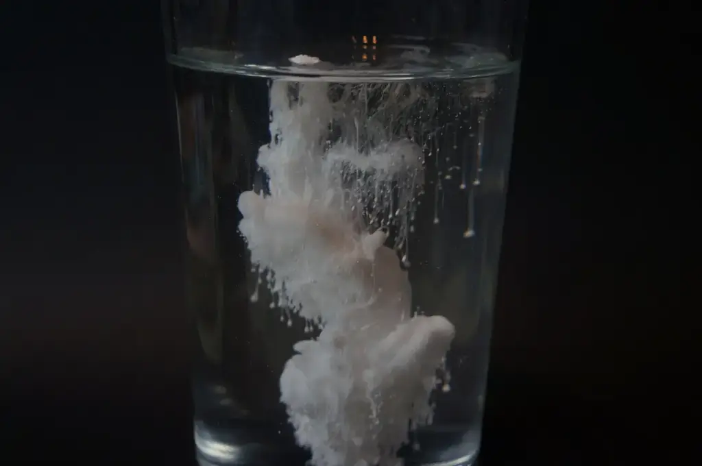 White titanium dioxide powder dispersing in a glass of water