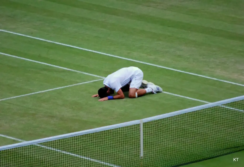 Novak Djokovic se agacha a comer un poco de hierba de la pista central de Wimbledon tras ganar su semifinal de 2011