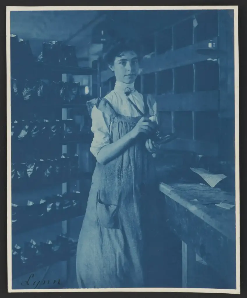 Trabajadora en una fábrica de calzado de Lynn (Massachusetts) en 1895, junto a estanterías llenas de piezas de zapatos, en una cianotipia de Frances Benjamin Johnston