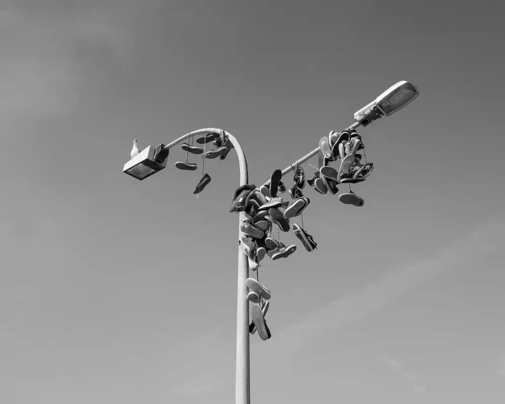 A street lamp in A Guarda, Spain, with dozens of old sneakers hanging from its arm, in black and white