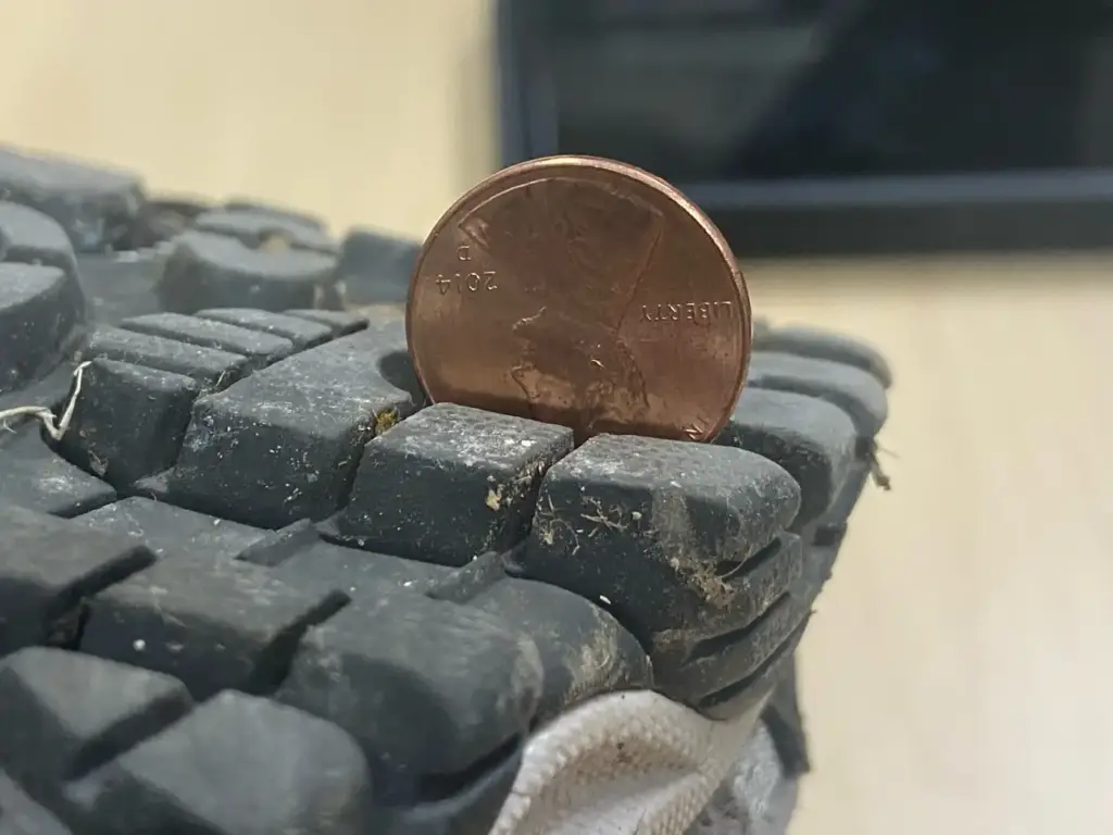 Moneda de un centavo metida de canto en el dibujo de la suela de una bota, usada por el Servicio de Parques Nacionales de Estados Unidos para ilustrar la profundidad de tacos exigida en una visita a una cueva