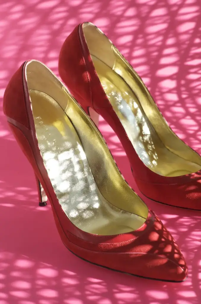 Par de zapatos de salón negros de charol con tacón alto, reflejados sobre una superficie brillante