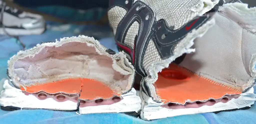 A worn-out running shoe cut in half, showing the white foam midsole and the orange insole