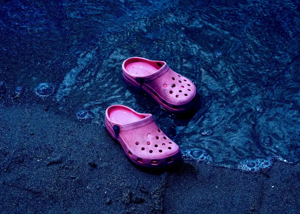 Un par de zuecos de espuma rosas flotando y mojados en la orilla del mar, de noche