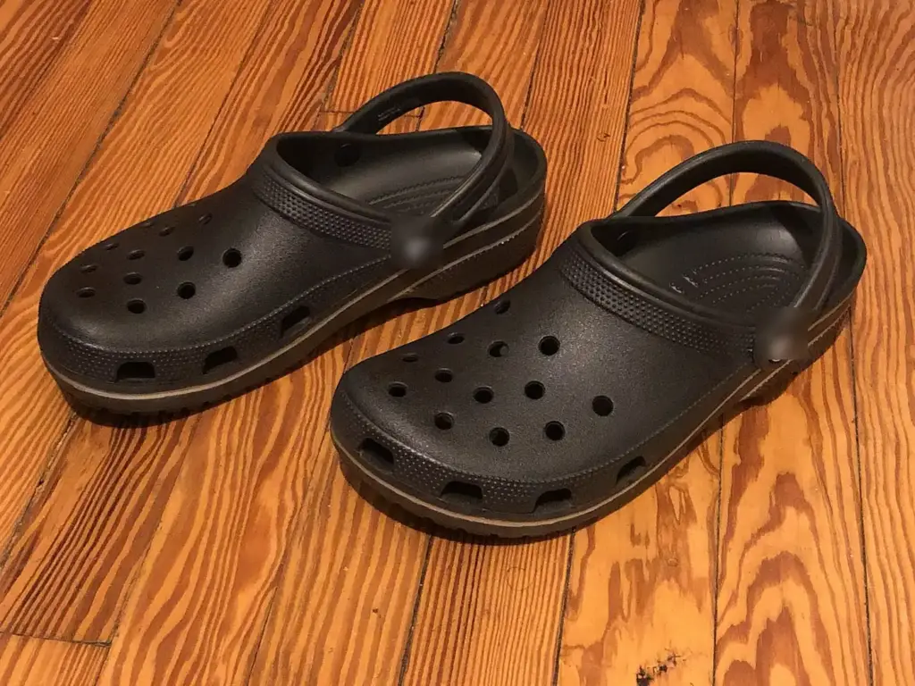 Zuecos de espuma negros sobre un suelo de madera, con los remaches de la tira difuminados